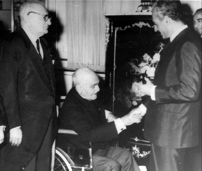 اینجا در این عکس، تقیزاده در آستانه ۹۰ سالگی است که دچار فلج پا شده و به اجبار بر رویِ صندلی چرخدار نشسته است. چند سال قبل در بزرگداشت او در دانشگاه کمبریج در لندن (۱۹۶۲م/سال ۱۳۴۱ش)، بزرگترین اندیشمندان ایرانشناس فرنگی اعتراف کردند که هیچ چیزی برایِ تقدیم به او نداریم که به معنایِ راستین لیاقت او را داشته باشد. با همین اعتراف بعد از سخنرانی والتر برونو هنینگ و هارولد بیلی دو ایرانشناس برجسته در وصف تقیزاده، کتاب مجموعه مقالات ایرانشناسی خود (۳۱ مقاله از خاورشناسان بهنام) به سه زبان فرانسه، آلمانی و انگلیسی با عنوان «رانِ ملخ» را به او پیشکش کردند. بهکارگیری اصطلاح «این رانِ ملخ تقدیم تو» در زبان فارسی به اظهار تواضع و فروتنی اشاره دارد (که ریشه تاریخی آن به داستان سلیمان نبی برمیگردد)؛ یعنی هدیهای که اگرچه به فردی داده میشود، ولی این هدیه در خور شان و مقام/جایگاه گیرنده هدیه نیست. حالا با این اوصاف، دردناکی این عکس در این است که محمدرضا پهلوی حتی حاضر نیست در برابر بزرگی این آدم (که علامه قزوینی او را حضرت تقیزاده مینامد) که به ناچار زمینگیر هم شده، کمی خم شود و از بالا با او دست ندهد.