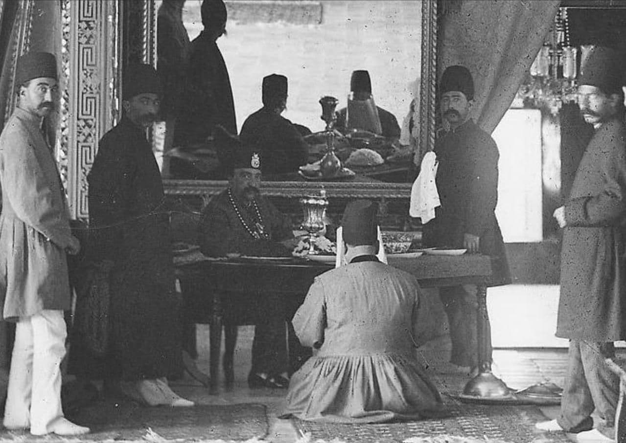 محمدحسنخانِ اعتمادالسلطنه -که رویِ زمین نشسته- برایِ ناصرالدینشاه در كاخ صاحبقرانيه روزنامه میخواند. او وزیر انطباعات (چاپونشر) و مترجم مخصوص شاه بود و ریاست دارالترجمه همایونی را نیز برعهده داشت.
اعتمادالسلطنه یک ماه پیش از کشتهشدنِ ناصرالدینشاه، در سن پنجاهوسه سالگی به علت سکته قلبی در تهران درگذشت.
*عكس از یوسفخان (نام عکاس را به اشتباه آنتوان سوریوگین نوشته بودم، که با تذکر دوست عزیزی آن را اصلاح کردم. گویا خیلی از عکسهایی که بهنام سوریوگین ثبت شده، متعلق به یوسفخان عکاسباشی دربار ناصری است).